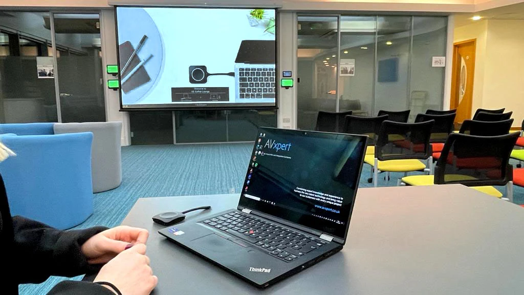 A laptop sharing to the room screen with a ClickShare button