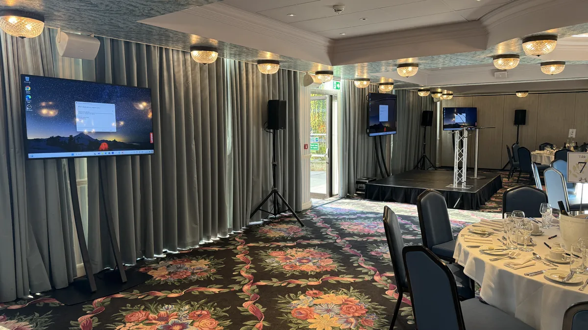 A function room set up by AV Xpert with a display screen and sound for a charity dinner