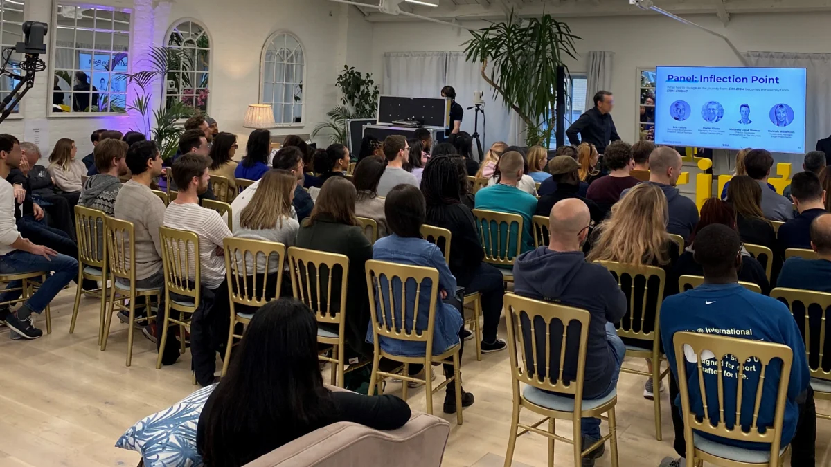 An audience at a hybrid event, with a camera and a screen showing remote speakers